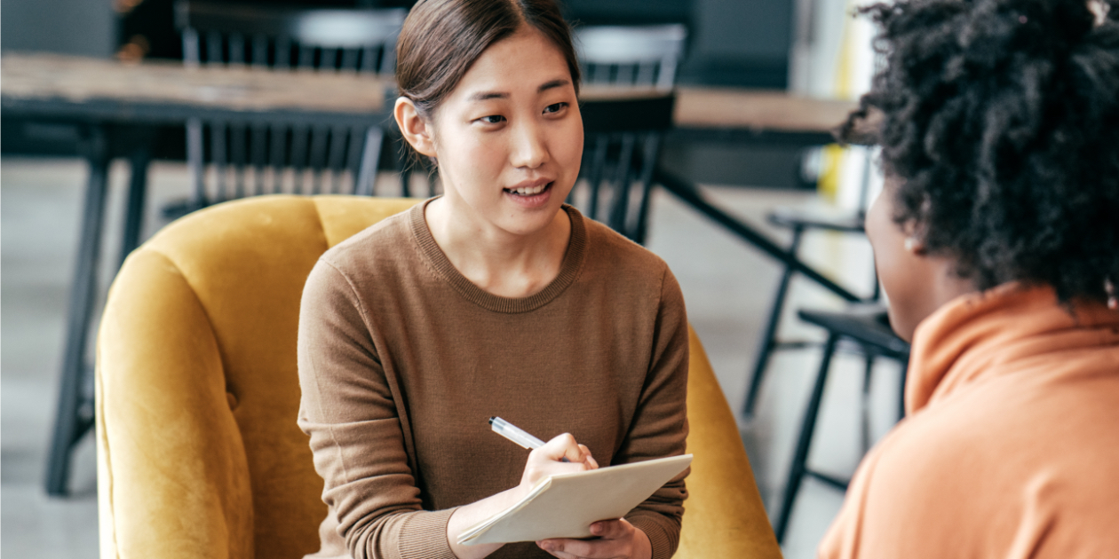 photo of woman holding a notebook and sitting down talking to another woman