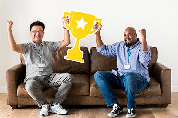 two employees siting on couch holding trophy