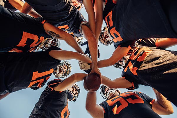 football players doing a huddle with hands on ball to show team unity and spirit